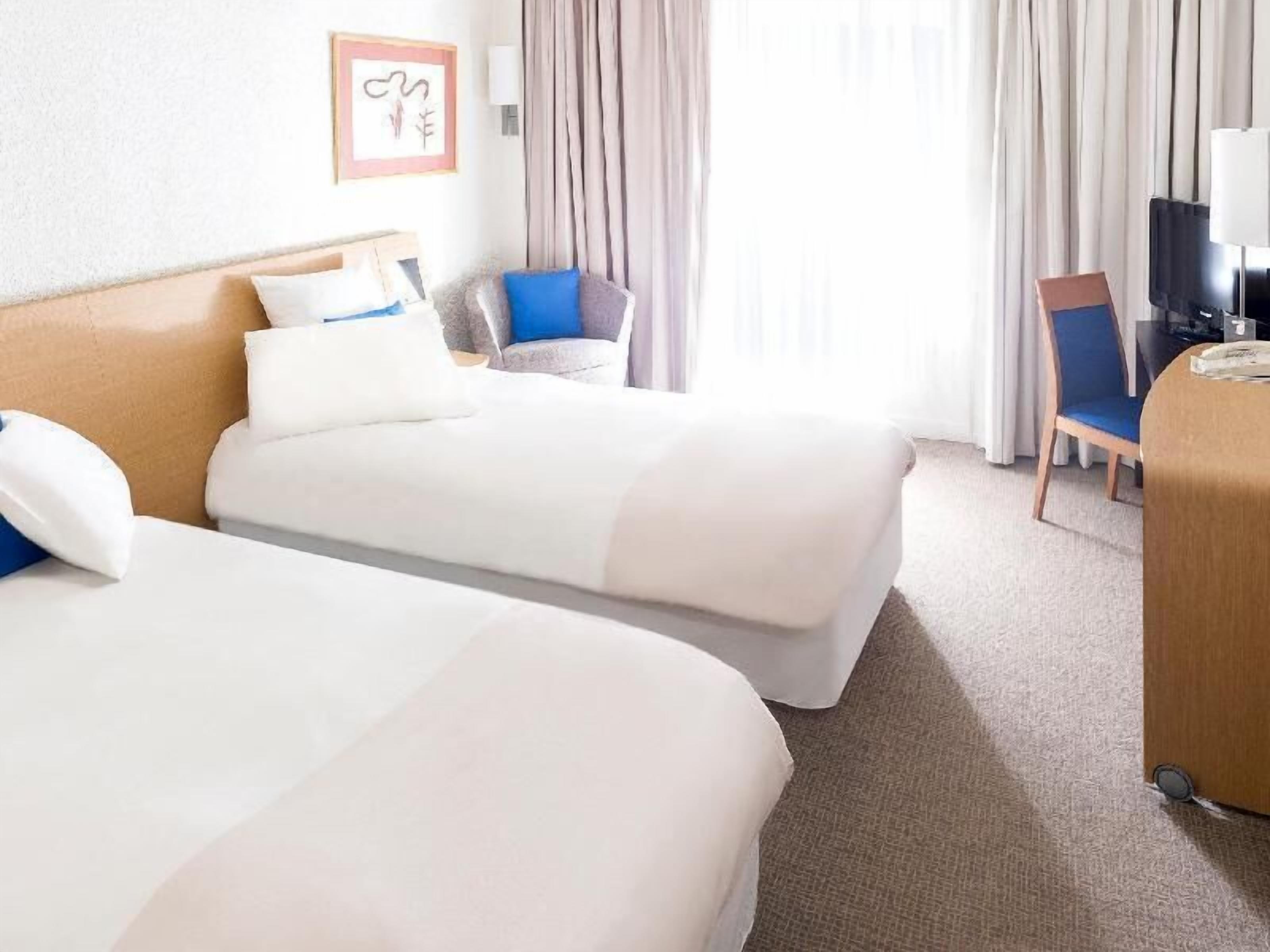 Une chambre d’hôtel avec deux lits, un bureau, une chaise et un téléviseur.
