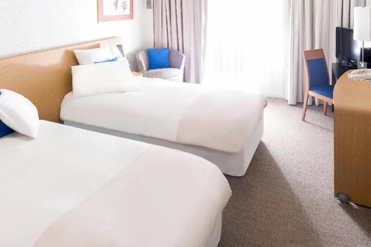 A hotel room with two beds, a desk, a chair, and a television.