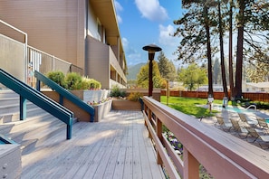 A wooden deck with a blue staircase, a pool area with lounge chairs, and a building with a balcony.