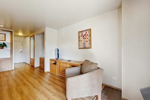 A room with a wooden floor, a desk with drawers, a chair, a television, and a framed picture on the wall.