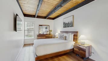 A bedroom with a wooden ceiling, a large bed, bedside tables, a mirror, and a window.