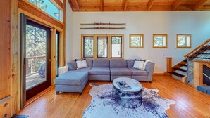 Uma sala de estar moderna com um amplo sofá de canto, uma mesa de centro redonda e teto de madeira.