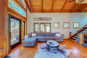 Ein modernes Wohnzimmer mit einer großen Eckcouch, einem runden Couchtisch und einer Holzbalkendecke.