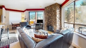 A living room with a stone fireplace, a large window, and a dining area with a table and chairs. - Comfortable, chic condo with mountain views - great Olympic Valley location (Squaw Valley)