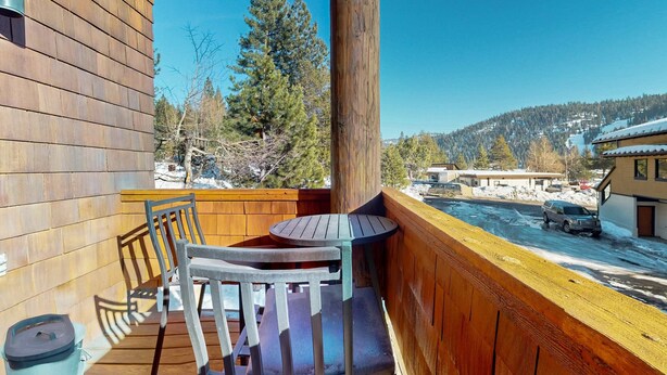 A wooden deck with a table and chairs, overlooking a snowy landscape and a building. - Comfortable, chic condo with mountain views - great Olympic Valley location (Squaw Valley)