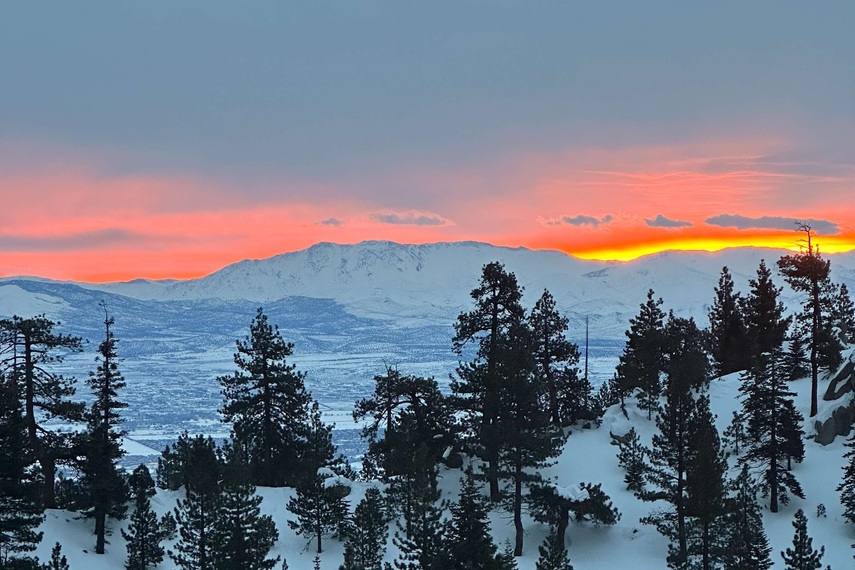 A snowy mountain landscape with trees and a sunset.