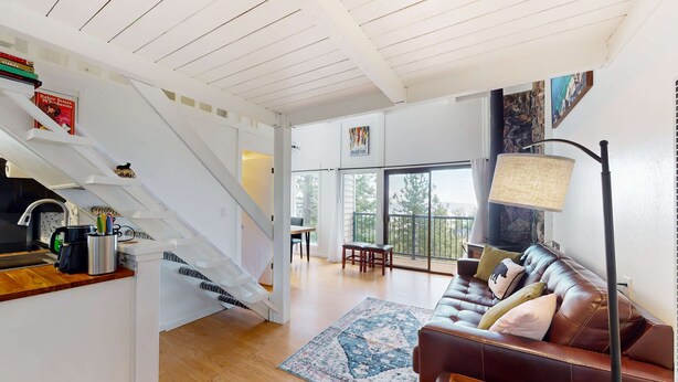 A modern living room with a staircase, a brown leather sofa, a patterned rug, and a dining area with a table and chairs.