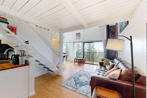 Una sala de estar moderna con una escalera, un sofá de cuero marrón, un tapete estampado y un comedor con mesa y sillas.