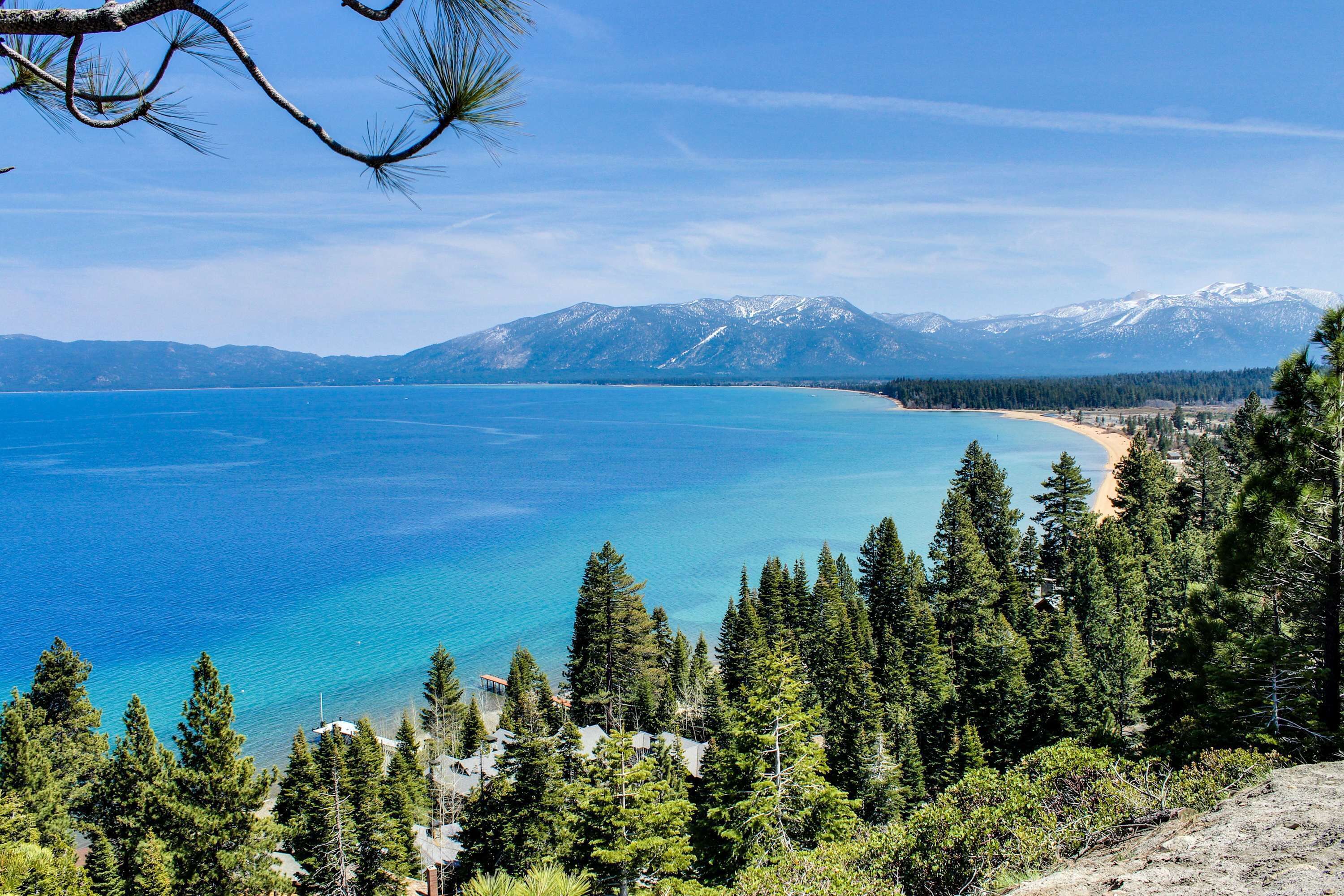 Eine Küstenlandschaft mit freiem Blick auf einen Strand, dichtem Wald und schneebedeckten Bergen im Hintergrund.