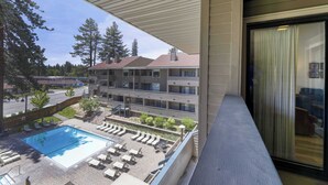 Ein Hotelbalkon mit Pool, Liegestühlen und Blick auf ein Mehrfamilienhaus.