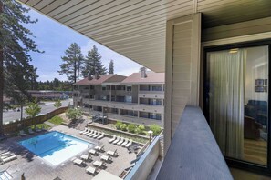 En hotellbalkong med en pool, solstolar och utsikt över en hög byggnad.