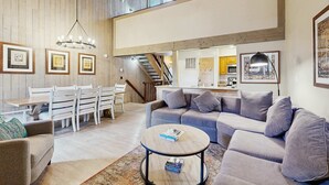 Un'ampia zona giorno con soffitto alto, un tavolo da pranzo con sedie, un divano, un tavolino da caffè e quadri appesi alle pareti.