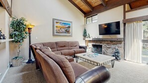 Una sala de estar acogedora con un sofá modular, una chimenea, un televisor y un ventanal grande.