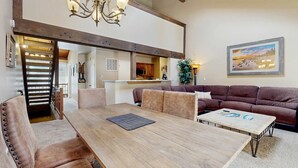Un salón espacioso con una mesa de comedor de madera, sillas de cuero, un sofá marrón y una lámpara de araña.