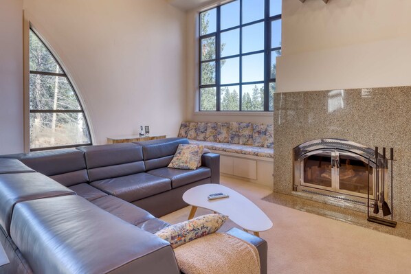 A modern living room with a leather sofa, a small coffee table, a fireplace, and large windows. - Unique circular home with wood fireplace, grill, & EV charger - dogs ok (Truckee)