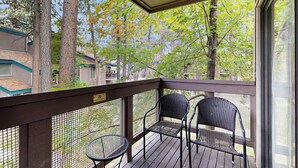 A covered outdoor area with two chairs and a small table, surrounded by a wooden deck and a mesh fence. - Cozy townhouse with pool access, deck, fireplace, and WiFi (South Lake Tahoe)