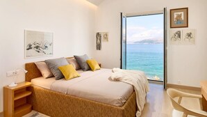 A bedroom with a bed, bedside table, chair, and a view of the sea. - Beachfront Stay With Private Pool (Supetar)
