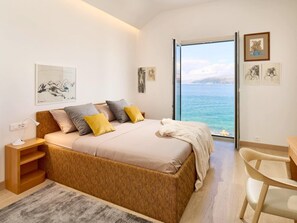 A bedroom with a bed, bedside table, chair, and a view of the sea. - Beachfront Stay With Private Pool (Supetar)
