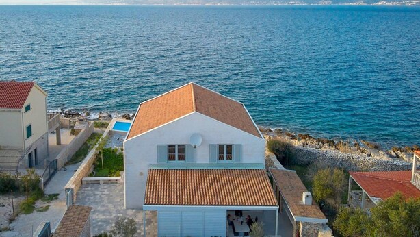 A coastal building with a tiled roof, a satellite dish, and a view of the sea and mountains in the background. - Beachfront Stay With Private Pool (Supetar)