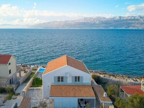 A coastal building with a tiled roof, a satellite dish, and a view of the sea and mountains in the background. - Beachfront Stay With Private Pool (Supetar)
