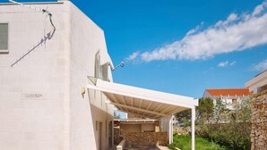 A modern building with a covered outdoor area, stone walls, and a clear blue sky. - Beachfront Stay With Private Pool (Supetar)