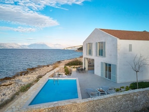 Ett modernt hus med pool, en uteplats och utsikt över havet.