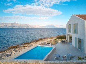 En modern byggnad med en pool och utomhusplats, med utsikt över en sjö eller ett annat vattendrag och berg.