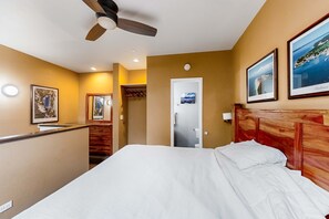 Een slaapkamer met een bed, een plafondventilator, een houten hoofdeinde en ingelijste foto's aan de muur.