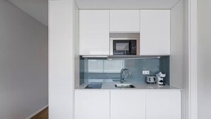 Una cocina compacta equipada con microondas, lavamanos y hervidor.