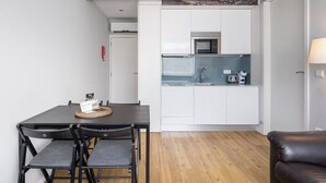Cocina compacta con armarios blancos, microondas y lavamanos. Hay una mesa de comedor con sillas y una alfombra pequeña.