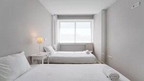 Habitación de hotel con dos camas, una ventana, una lámpara y una mesita.