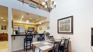 A dining area with a wooden table and chairs, a chandelier, and a kitchen in the background. - Centrally located condo with pool, tennis, hot tubs, & fireplace - near skiing (Squaw Valley)