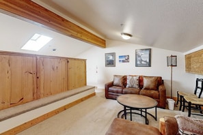 A spacious living area with a wooden staircase, a leather sofa, a round coffee table, and a dining table with chairs. - Centrally located condo with pool, tennis, hot tubs, & fireplace - near skiing (Squaw Valley)