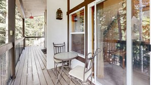 A wooden deck with a table and chairs, a glass door, and a view of trees. - Centrally located condo with pool, tennis, hot tubs, & fireplace - near skiing (Squaw Valley)
