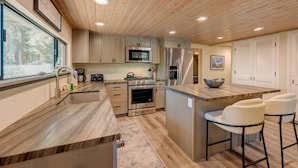A modern kitchen with wooden ceiling, stainless steel appliances, and a large island with bar stools. - A-frame home with large deck, game room, wood fireplace & near the lake - dogs ok (Carnelian Bay)