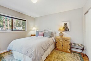 Ein Schlafzimmer mit einem Bett, Nachttischen, einer Lampe, einer Bank, einem Teppich und einem Fenster mit Blick auf Bäume.