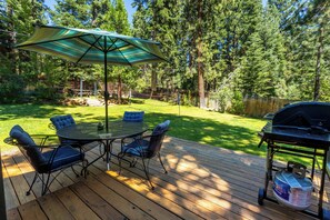 A deck with a round table and chairs, an umbrella, and a grill. - Welcoming home near the lake with furnished deck & large, enclosed yard (Tahoe Vista)