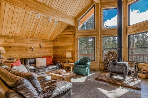 L’intérieur d’une cabane en rondins, avec une chambre à coucher en mezzanine, des murs en bois, une cheminée, des meubles en cuir et de grandes fenêtres.