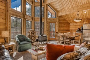 Un intérieur de chalet chaleureux avec une cheminée, des meubles en bois et de grandes fenêtres.