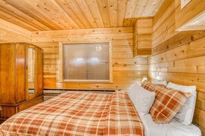 L’intérieur d’un chalet en bois, avec un lit, une fenêtre équipée de stores et une armoire en bois.