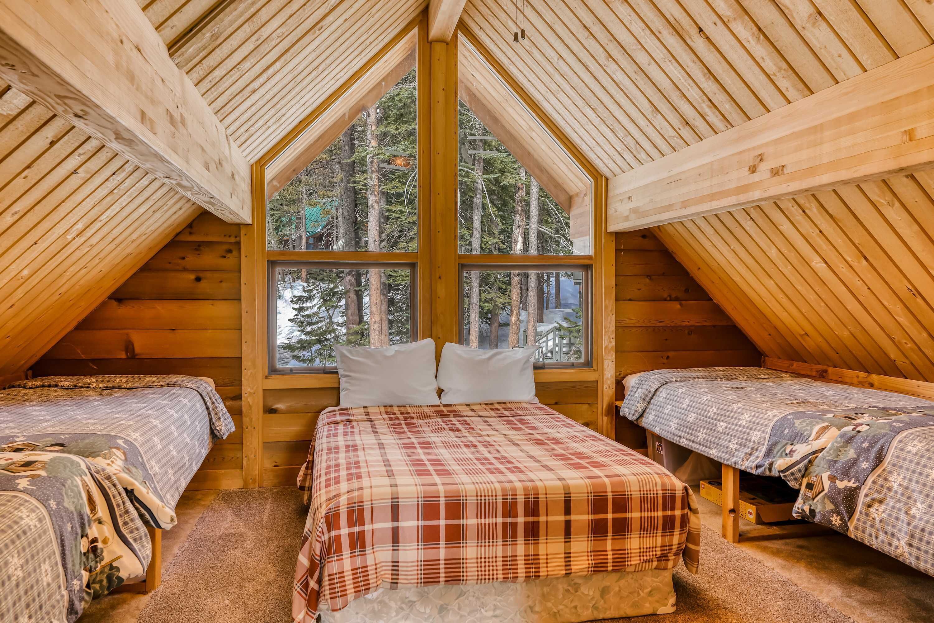Ein gemütliches Schlafzimmer im Dachgeschoss mit zwei Betten, einem großen Fenster und Holzbalken.