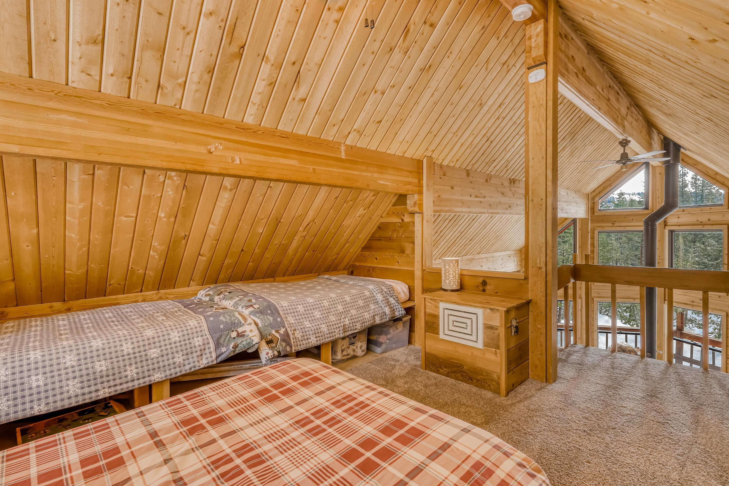 Ein Schlafzimmer einer Holzhütte mit Schlafkoje, Nachttisch und Fenster mit Blick ins Freie.
