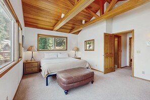 A bedroom with a bed, bedside lamps, a wooden bench, a window, and a door. - Terrific lakefront gem with private hot tub, dock & beach - near skiing & town (Truckee)
