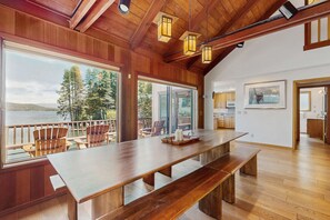A spacious room with a large wooden table, multiple chairs, and a view of a lake. - Terrific lakefront gem with private hot tub, dock & beach - near skiing & town (Truckee)