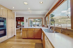 A kitchen with wooden cabinets, a double sink, and a large window offering a view of a mountainous landscape. - Terrific lakefront gem with private hot tub, dock & beach - near skiing & town (Truckee)