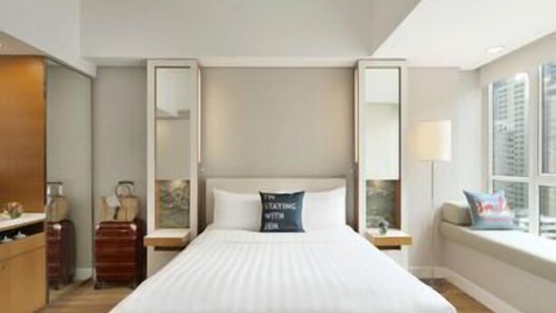 Une chambre d’hôtel avec un grand lit, une table de chevet, une commode, un miroir et une fenêtre donnant sur un beau paysage.