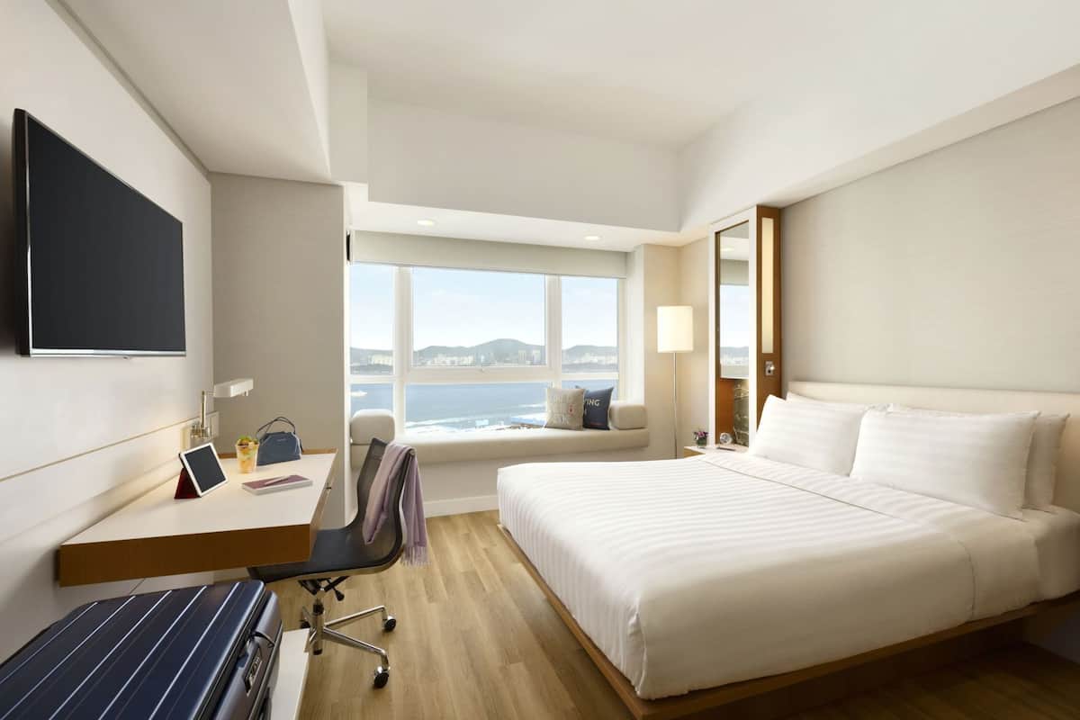 A hotel room with a bed, desk, chair, TV, and a window with a view.