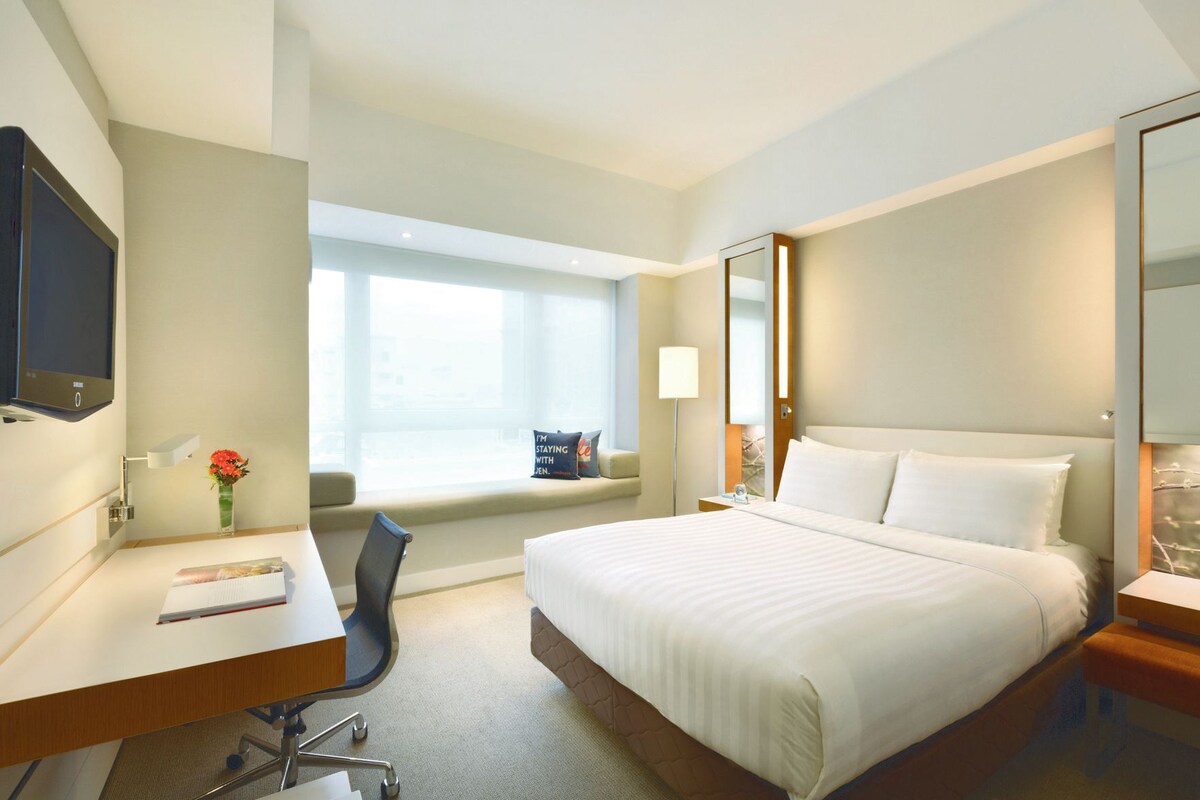 Ein Hotelzimmer mit Bett, Schreibtisch, Stuhl, Fernseher und einem Fenster mit Blick.
