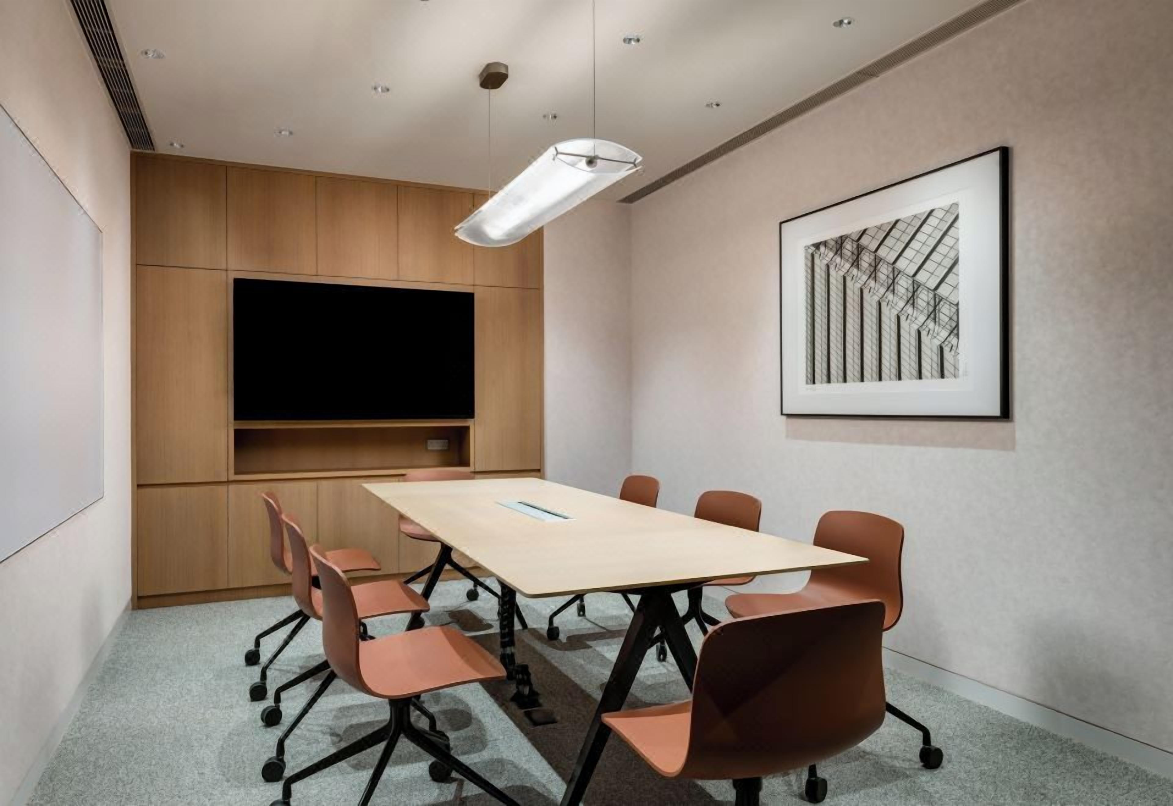 A conference room with a long table, six chairs, a mounted TV, and a framed architectural drawing on the wall.