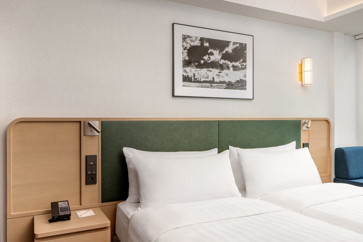 Ein Hotelzimmer mit einem Bett, einem Nachttisch, einem Telefon und einem gerahmten Bild an der Wand.